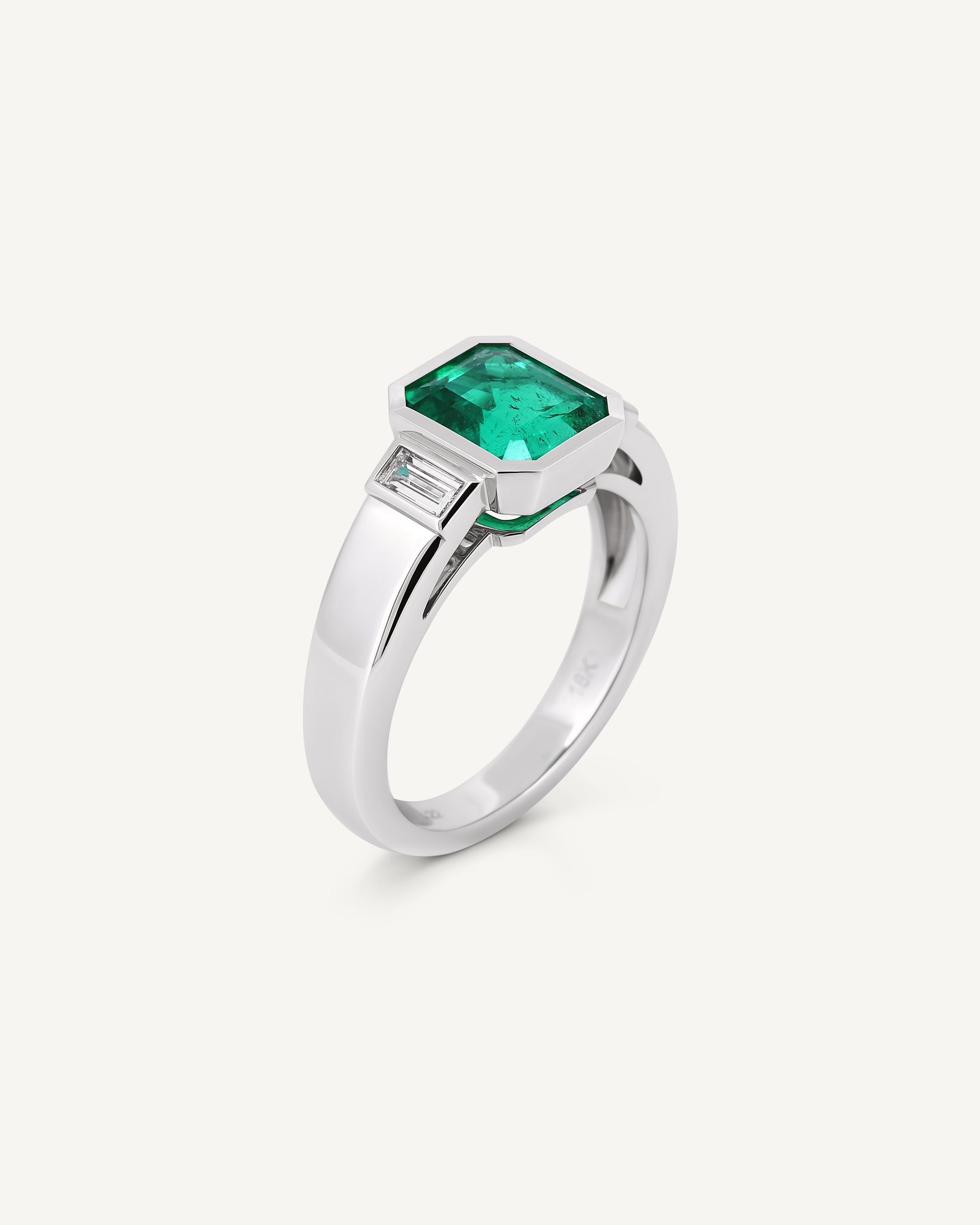 Bezel-set emerald ring with baguette diamond accents, three-quarter view