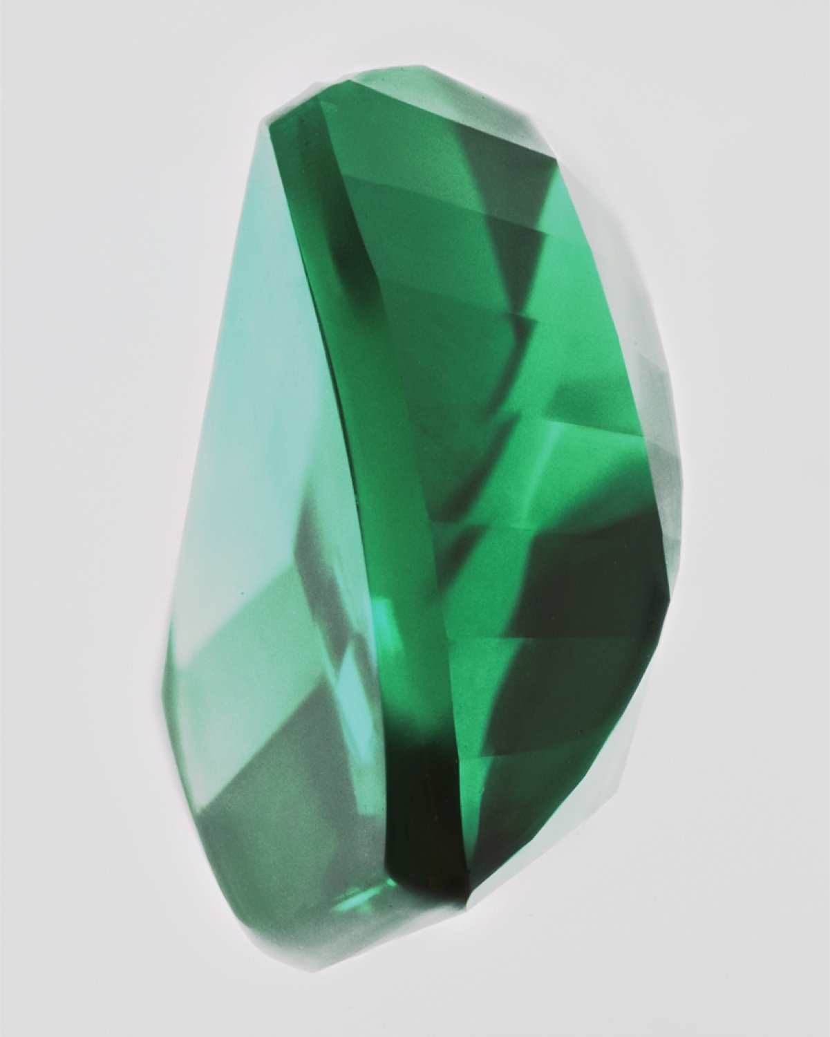 A close-up of a faceted green gemstone, its cut planes catching the light