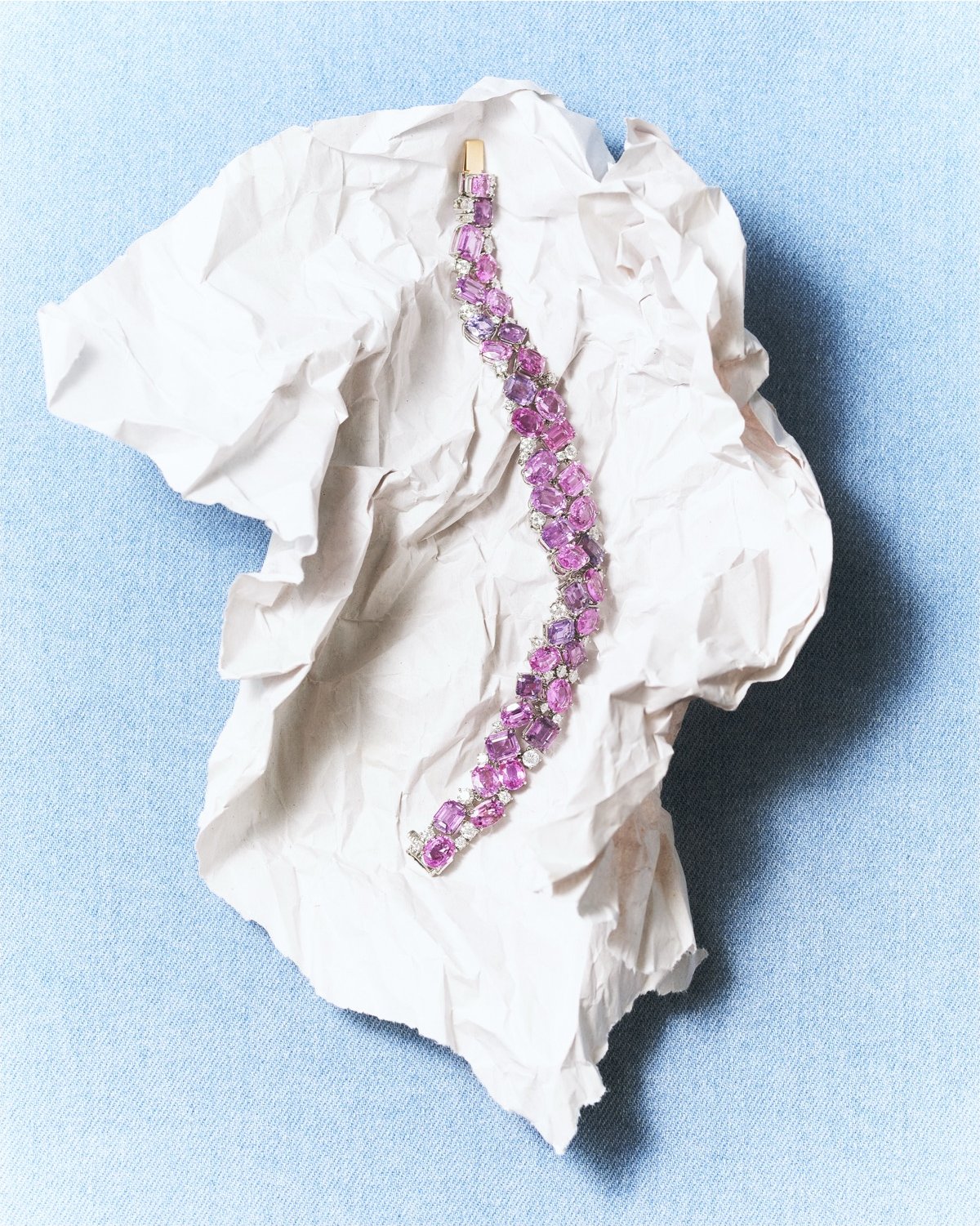 A pink sapphire and diamond bracelet resting on crumpled paper, the finished piece
